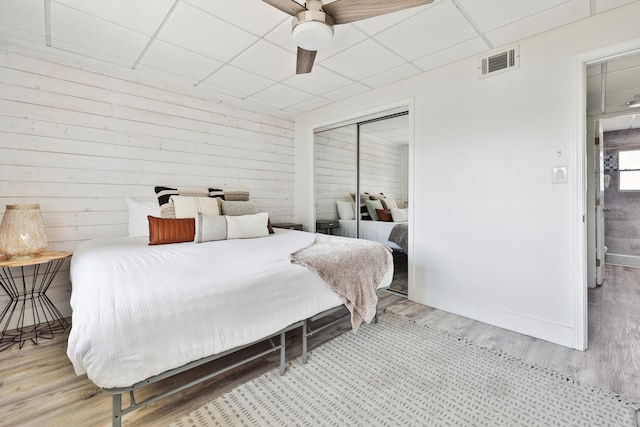 bedroom with ceiling fan, a drop ceiling, light wood-type flooring, and a closet