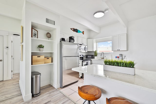 kitchen featuring a kitchen bar, light stone countertops, white cabinetry, and appliances with stainless steel finishes