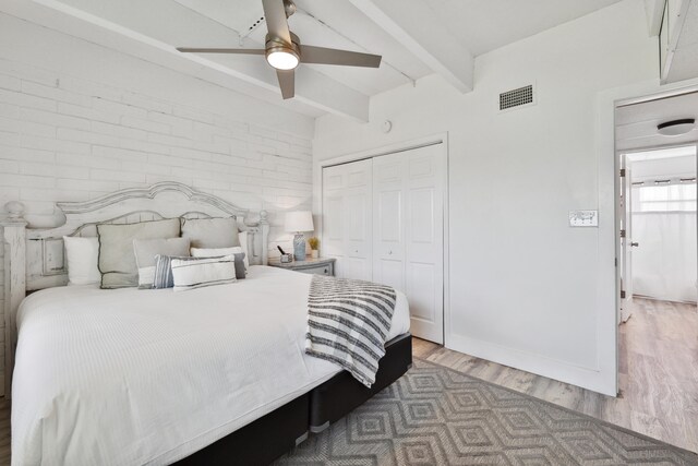 bedroom featuring brick wall, ceiling fan, beam ceiling, hardwood / wood-style floors, and a closet