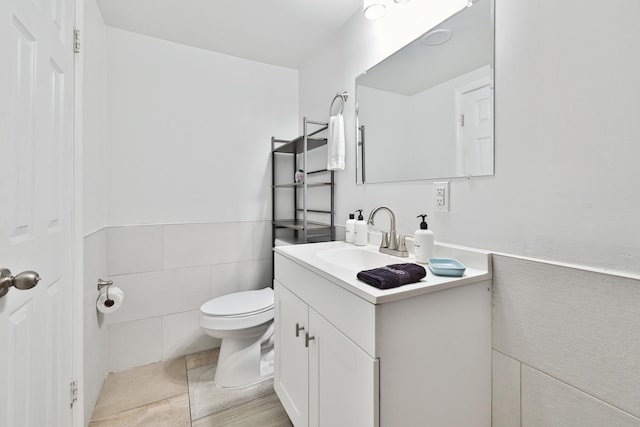 bathroom with vanity, toilet, and tile walls