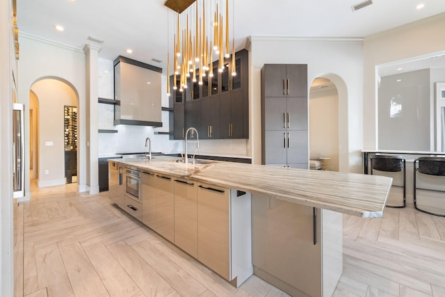 kitchen with pendant lighting, an island with sink, sink, oven, and light parquet floors