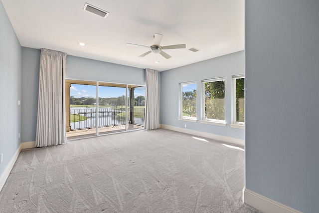 carpeted empty room with a water view and ceiling fan