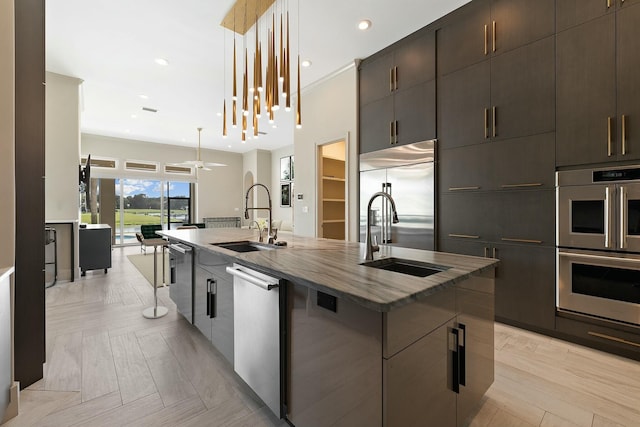 kitchen featuring appliances with stainless steel finishes, decorative light fixtures, sink, and a center island with sink