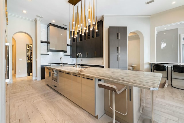 kitchen featuring a kitchen bar, sink, hanging light fixtures, a kitchen island with sink, and light parquet floors