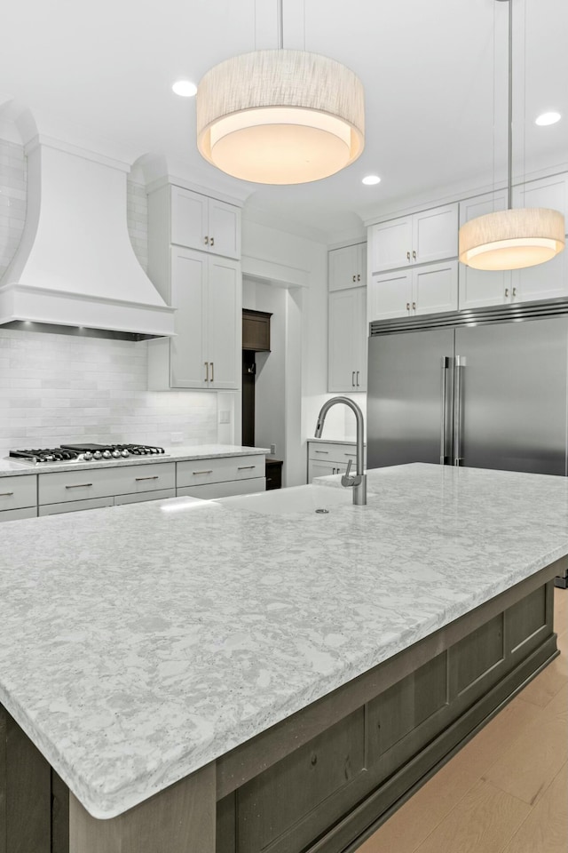 kitchen featuring white cabinets, appliances with stainless steel finishes, hanging light fixtures, and custom exhaust hood