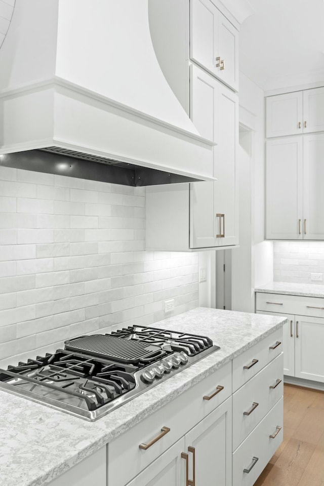 kitchen featuring backsplash, stainless steel gas stovetop, white cabinets, custom range hood, and light wood-type flooring