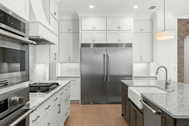 kitchen with premium range hood, white cabinetry, stainless steel appliances, and decorative light fixtures