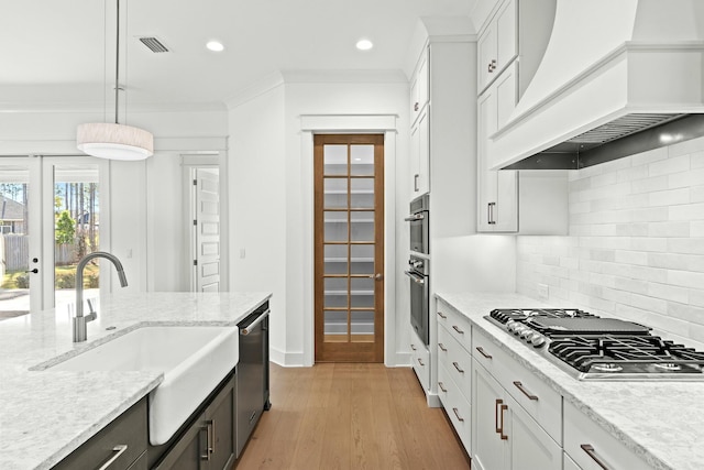 kitchen featuring appliances with stainless steel finishes, premium range hood, white cabinetry, and sink