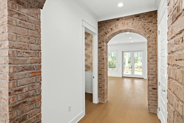 corridor with light hardwood / wood-style flooring, brick wall, and ornamental molding