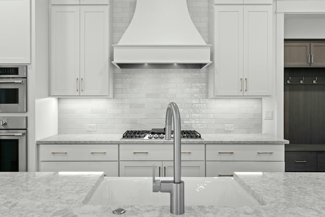 kitchen with backsplash, white cabinetry, light stone counters, and custom exhaust hood