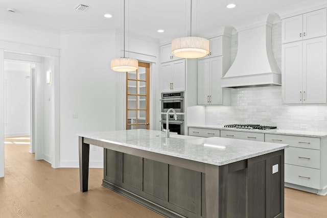 kitchen featuring premium range hood, decorative backsplash, a kitchen island with sink, and pendant lighting