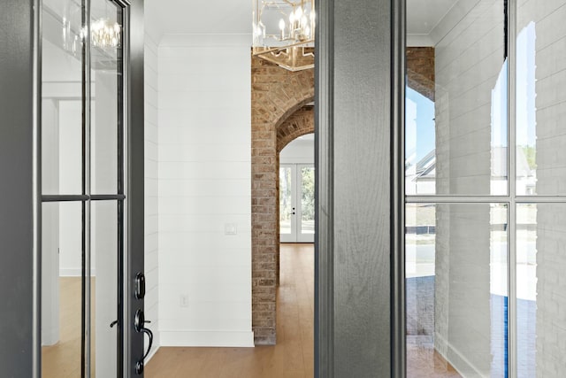 corridor featuring french doors, a notable chandelier, and hardwood / wood-style flooring