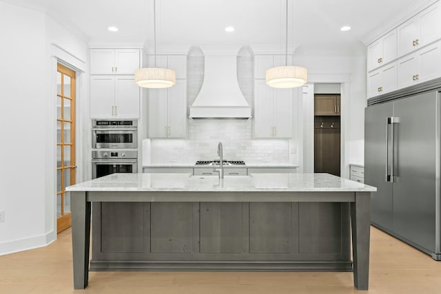 kitchen featuring pendant lighting, custom exhaust hood, stainless steel appliances, and a kitchen island with sink