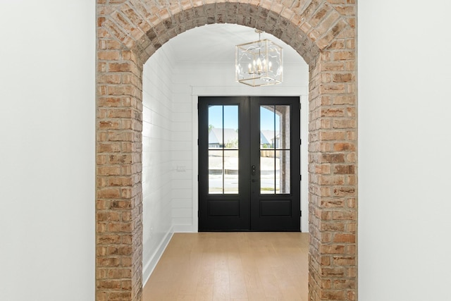 entryway with crown molding, french doors, light wood-type flooring, and a notable chandelier