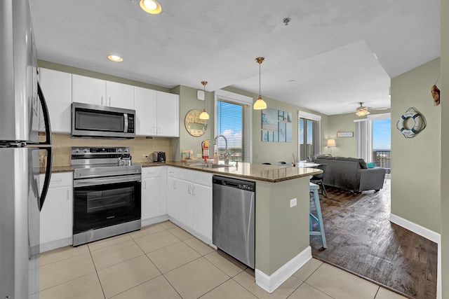 kitchen featuring sink, white cabinetry, stainless steel appliances, decorative light fixtures, and kitchen peninsula