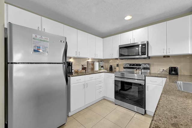 kitchen with light tile patterned flooring, appliances with stainless steel finishes, white cabinets, and a textured ceiling