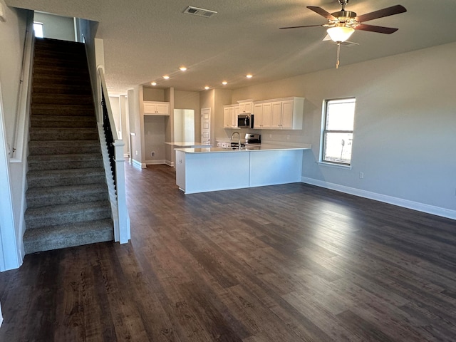 kitchen featuring dark wood-type flooring, white cabinets, ceiling fan, appliances with stainless steel finishes, and kitchen peninsula