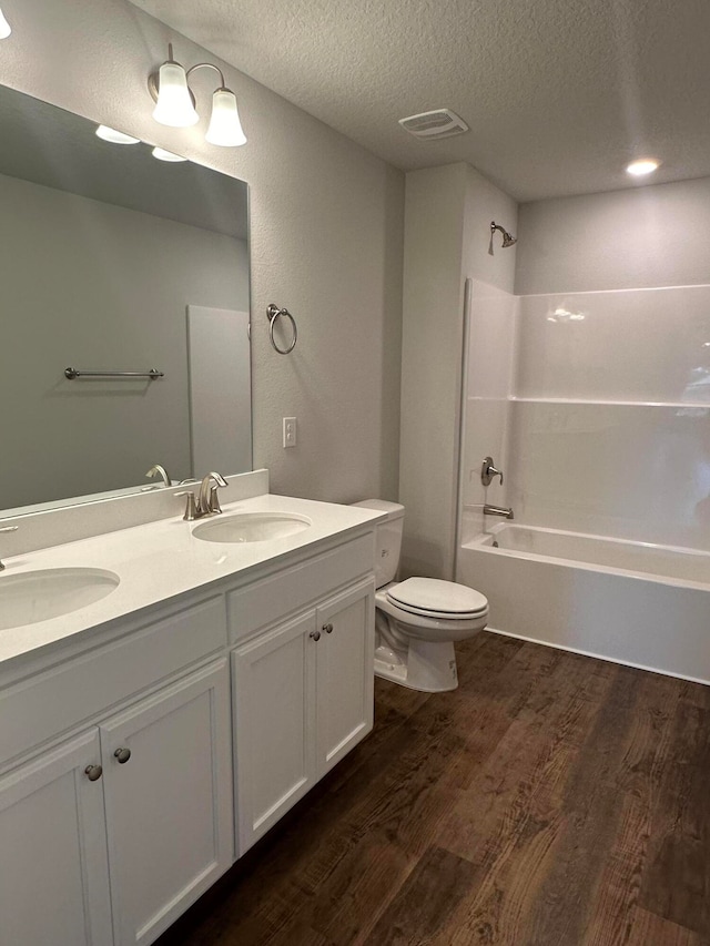 full bathroom with a textured ceiling, vanity, washtub / shower combination, hardwood / wood-style floors, and toilet