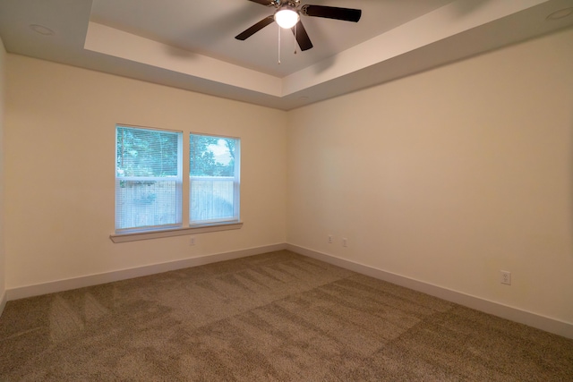 carpeted empty room with a raised ceiling and ceiling fan