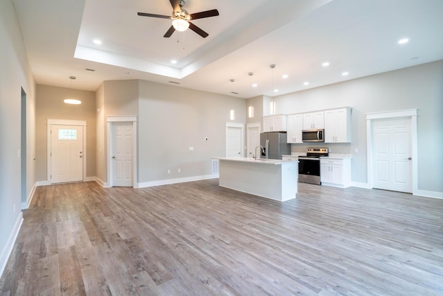 kitchen featuring white cabinets, a center island with sink, hanging light fixtures, light hardwood / wood-style flooring, and stainless steel appliances