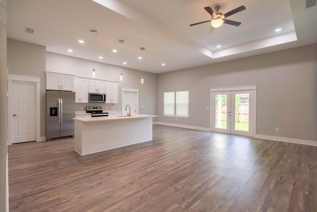 kitchen featuring stainless steel appliances, decorative light fixtures, hardwood / wood-style flooring, a center island with sink, and white cabinets