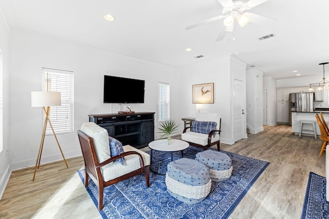 living room featuring ceiling fan with notable chandelier, light hardwood / wood-style floors, and crown molding