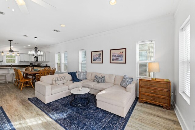 living room with light hardwood / wood-style flooring, crown molding, and ceiling fan with notable chandelier