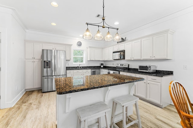 kitchen with a kitchen island, stainless steel appliances, white cabinets, and light hardwood / wood-style flooring