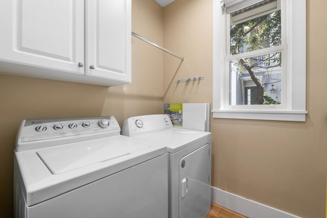 clothes washing area with separate washer and dryer and cabinets