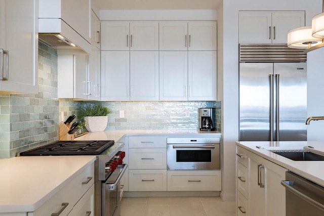 kitchen featuring white cabinets, backsplash, premium appliances, and light tile floors