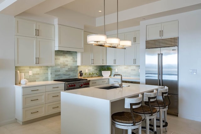 kitchen featuring high quality appliances, a center island with sink, decorative light fixtures, backsplash, and sink