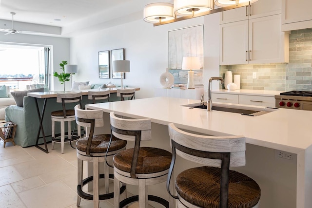 kitchen featuring backsplash, a kitchen bar, white cabinetry, sink, and light tile floors