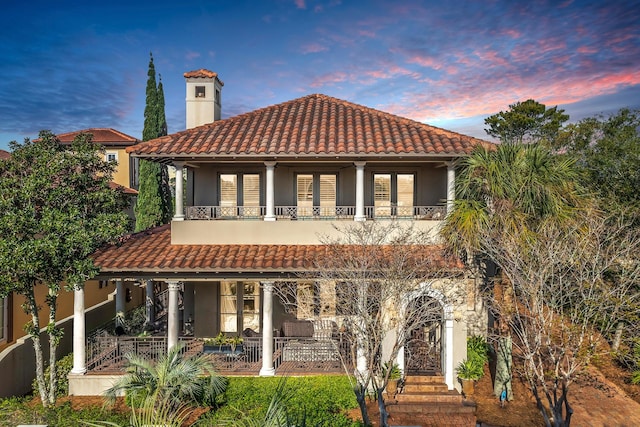 back house at dusk featuring a porch and a balcony