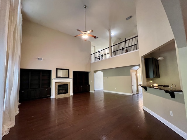 unfurnished living room featuring dark hardwood / wood-style floors, a tile fireplace, a towering ceiling, and ceiling fan