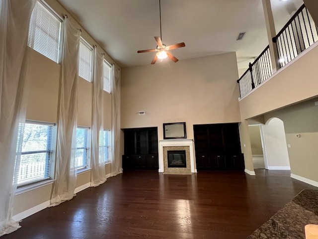 unfurnished living room with ceiling fan, a towering ceiling, a fireplace, and dark hardwood / wood-style flooring