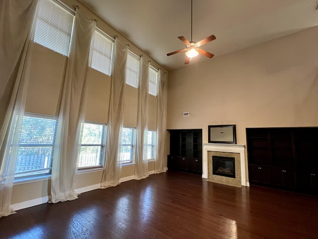 unfurnished living room with a towering ceiling, dark wood-type flooring, and ceiling fan