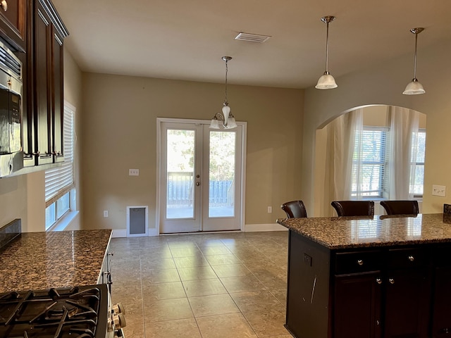 kitchen featuring french doors, decorative light fixtures, dark brown cabinets, and dark stone countertops