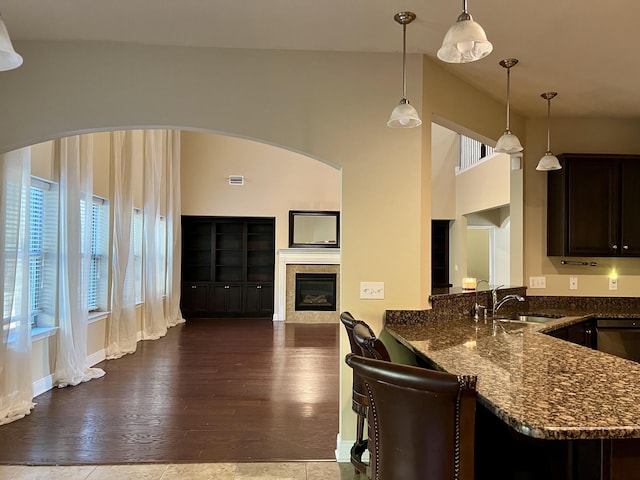 kitchen with a tile fireplace, pendant lighting, sink, dark stone countertops, and dark brown cabinetry