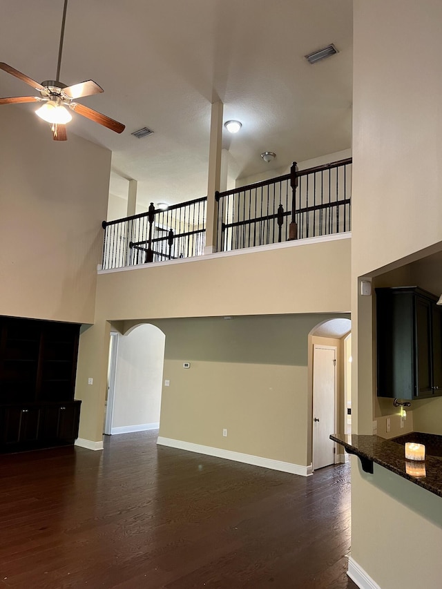 unfurnished living room with a towering ceiling, dark hardwood / wood-style floors, and ceiling fan