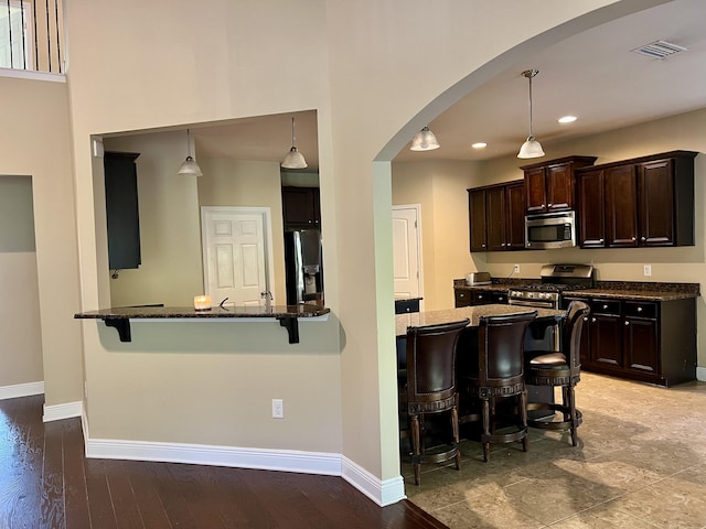 kitchen with dark brown cabinetry, appliances with stainless steel finishes, a breakfast bar, and hanging light fixtures