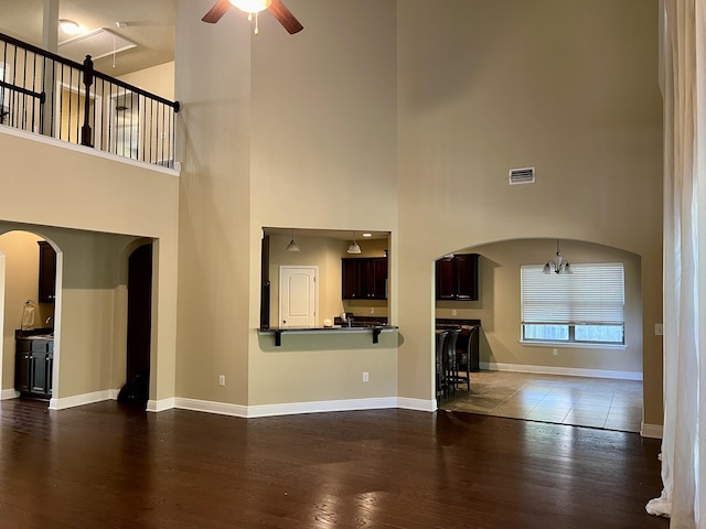 unfurnished living room with wood-type flooring, ceiling fan with notable chandelier, and a high ceiling