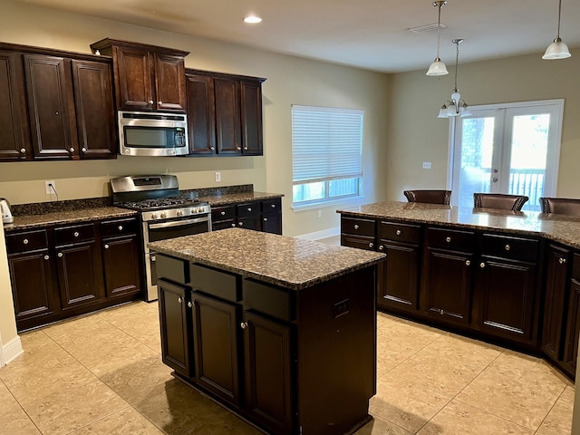 kitchen featuring appliances with stainless steel finishes, pendant lighting, dark stone countertops, a center island, and dark brown cabinetry