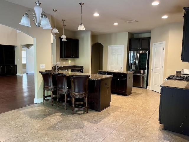 kitchen with pendant lighting, stainless steel fridge, light stone counters, a kitchen island, and kitchen peninsula