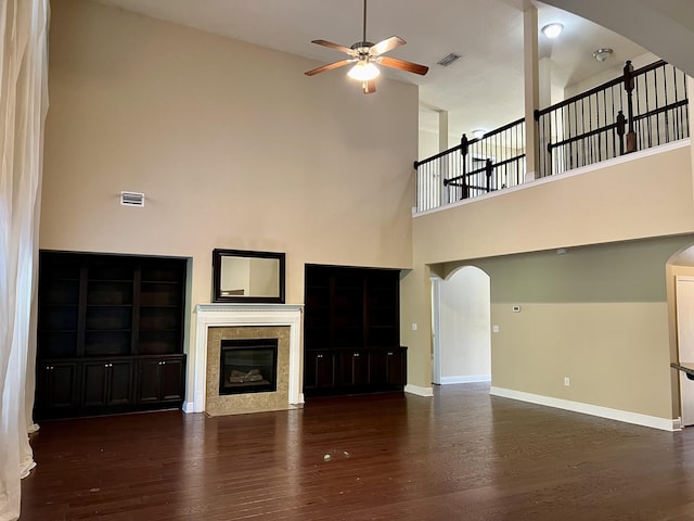 unfurnished living room featuring a high ceiling, a tiled fireplace, dark hardwood / wood-style flooring, and ceiling fan