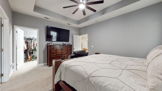 carpeted bedroom with ceiling fan, a closet, a spacious closet, and a tray ceiling