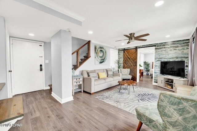 living room featuring light wood-type flooring, a barn door, ceiling fan, and crown molding