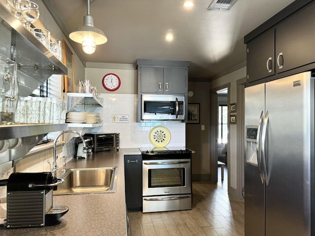 kitchen with backsplash, stainless steel appliances, sink, light hardwood / wood-style flooring, and hanging light fixtures