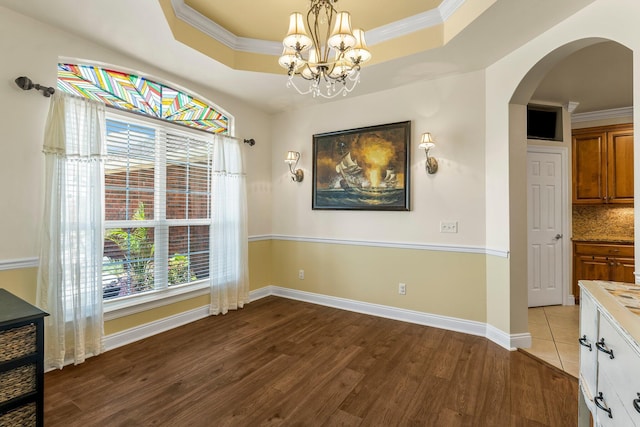 dining area with hardwood / wood-style flooring, a raised ceiling, crown molding, and an inviting chandelier