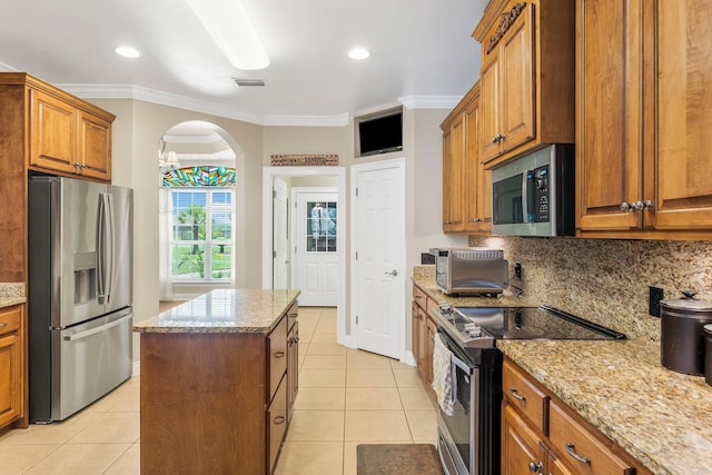 kitchen featuring light stone countertops, a center island, stainless steel appliances, light tile patterned flooring, and ornamental molding