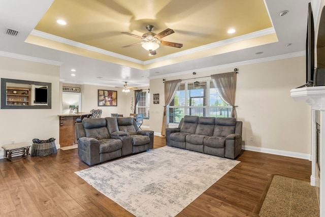 living room featuring wood-type flooring, a tray ceiling, and crown molding